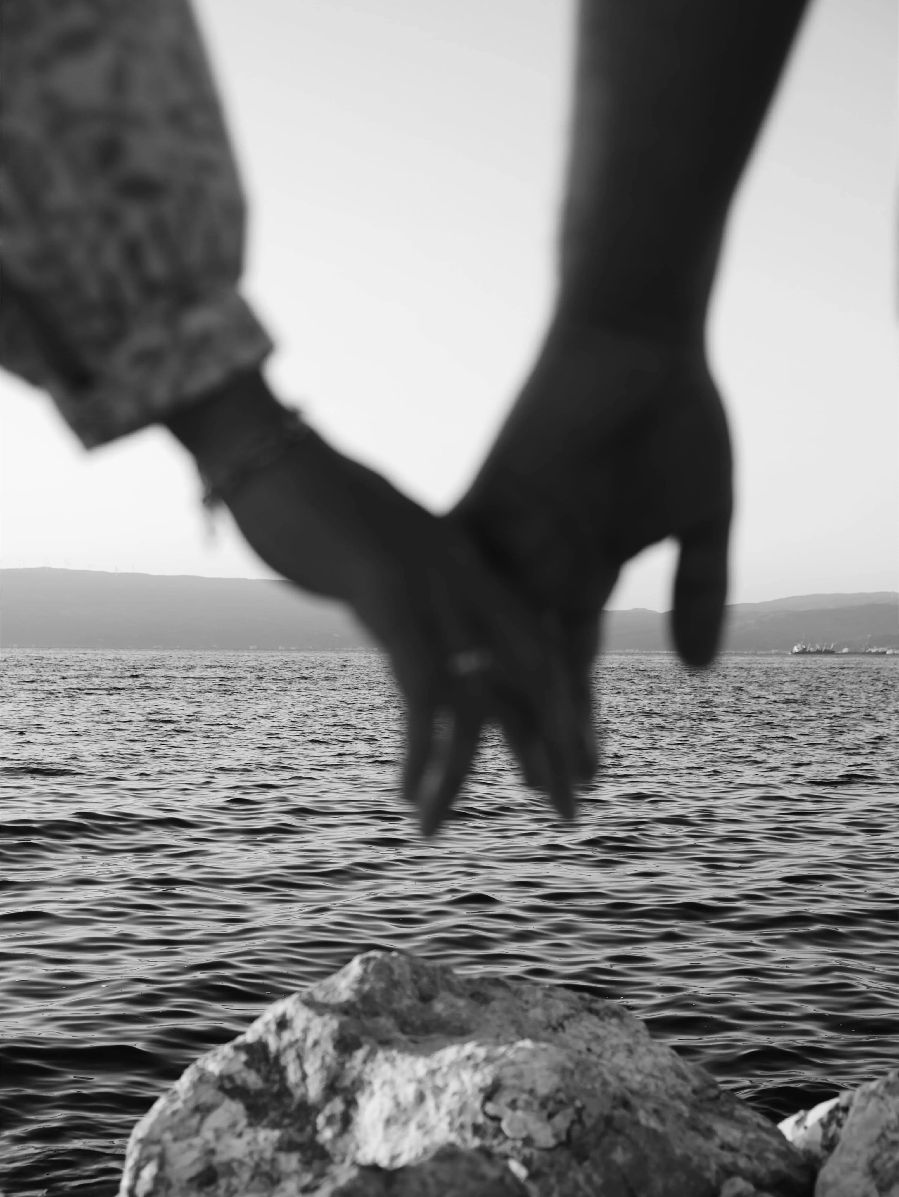 Two hands holding with the ocean behind them
