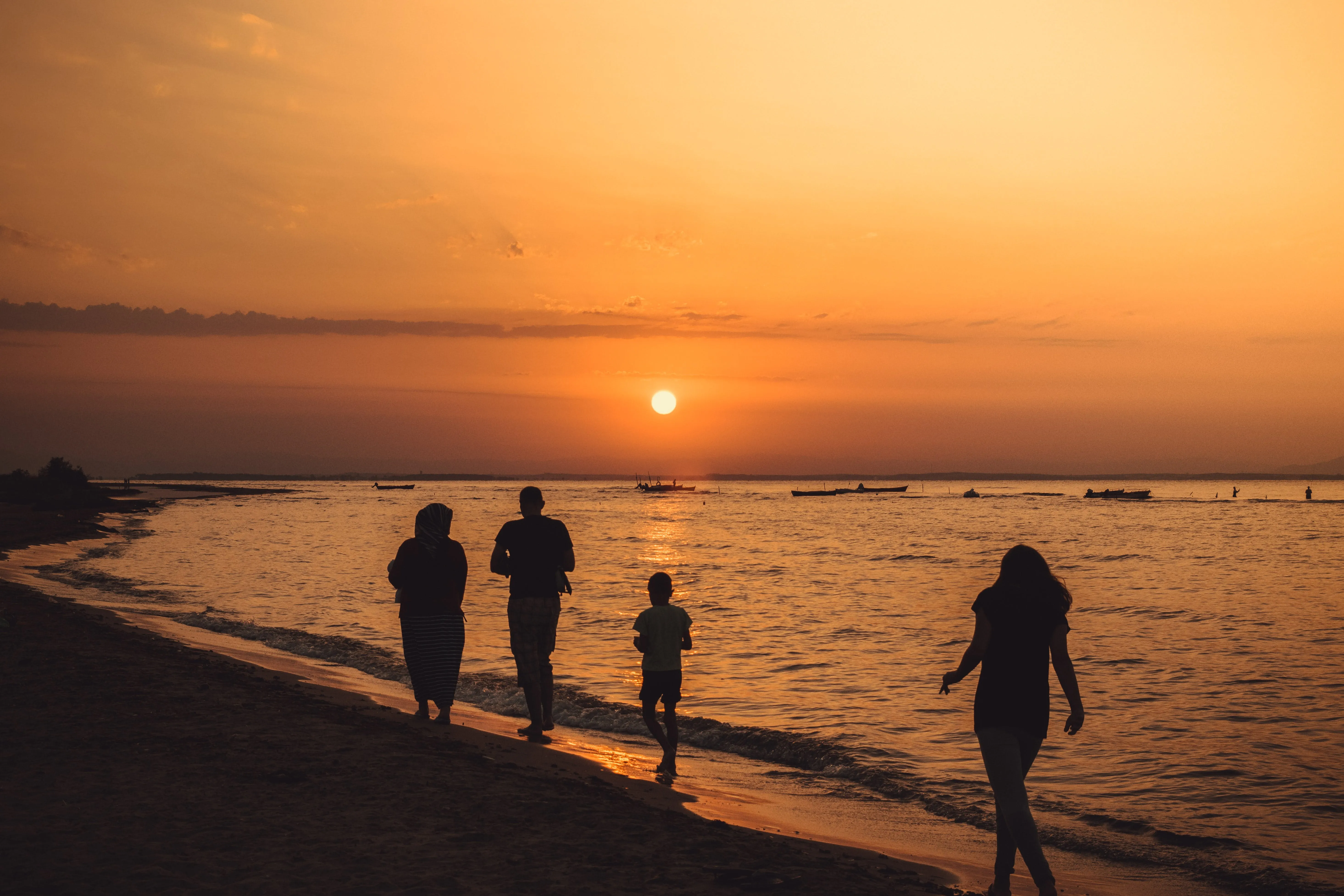 A family walking down the beach whilst the sun is setting in the distance